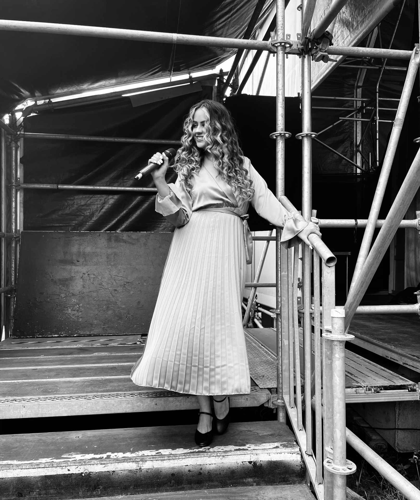 Chloe with her microphone on the stage steps, in black and white